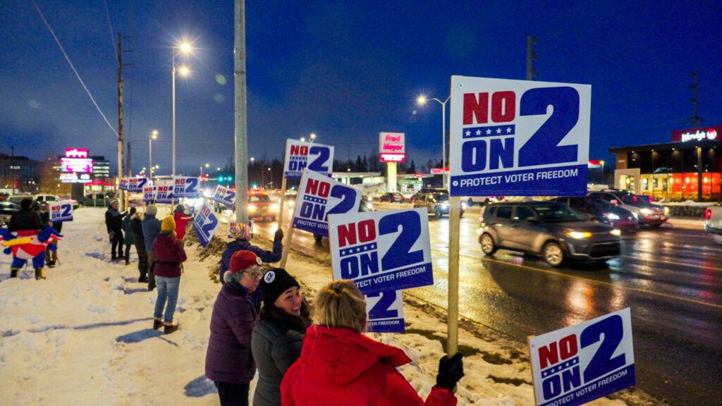 People standing outside holding signs against reading "NO ON 2 PROTECT VOTER FREEDOM"
