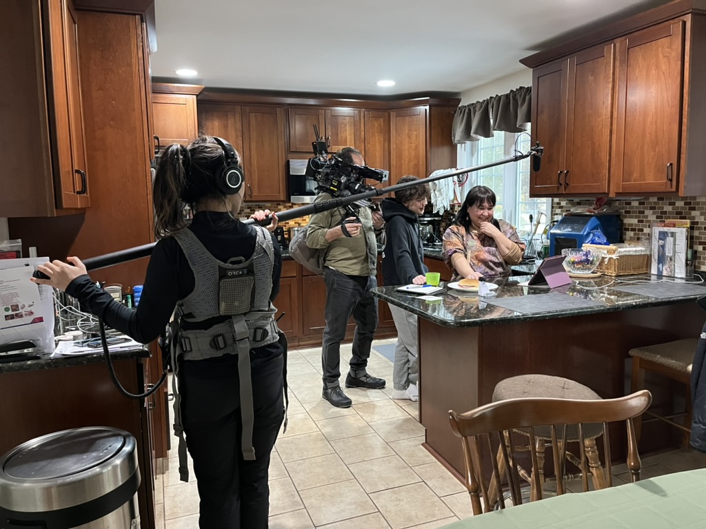 People vs. Politics crew films Michelle Spark and her son in their kitchen, with a cameraman and boom operator positioned to capture the scene.