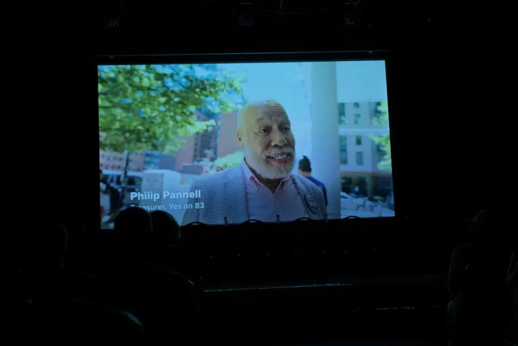 A still from People vs. Politics projected on screen, featuring Philip Pannell.